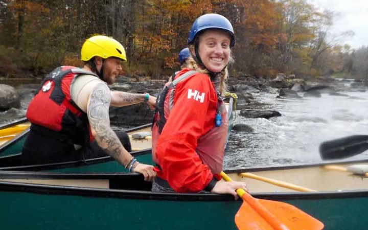 a person in a canoe smiles as another person in another canoe holds on to the first one
